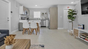 Una cocina moderna con armarios blancos, un microondas y una zona de comedor con sillas blancas.