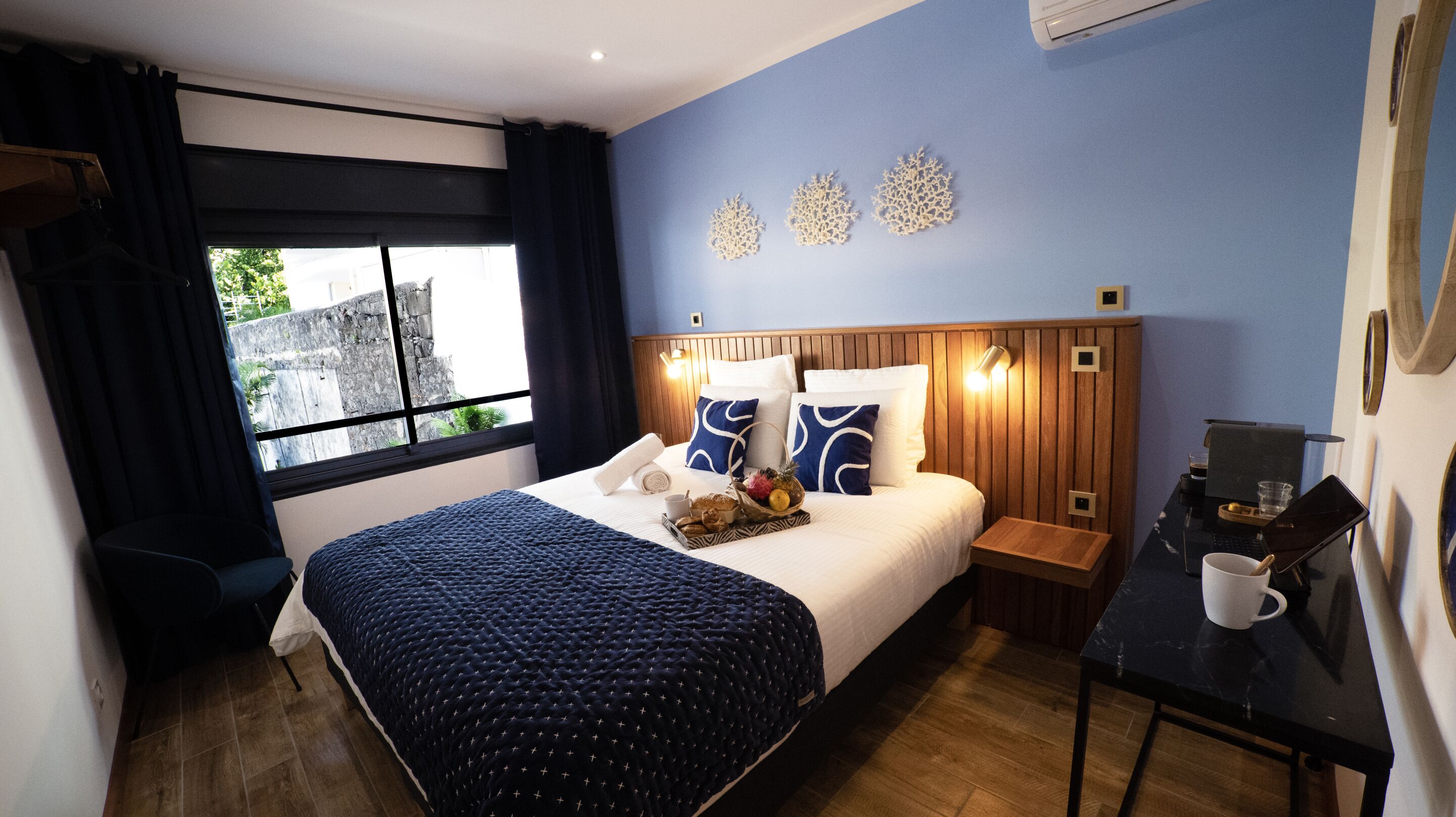 Ein Hotelzimmer mit Bett, Schreibtisch, Stuhl, einem Fenster mit Vorhängen und Wanddekoration.