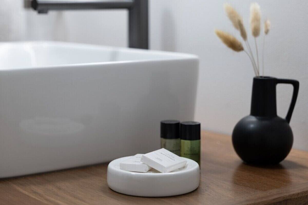 A bathroom with a white bathtub, a small white soap dish, a black vase with pampas grass, and two bottles of liquid soap.