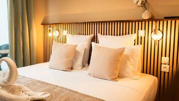 A hotel room with a bed, pillows, a bedside table, a vase with flowers, and a towel on the bed.