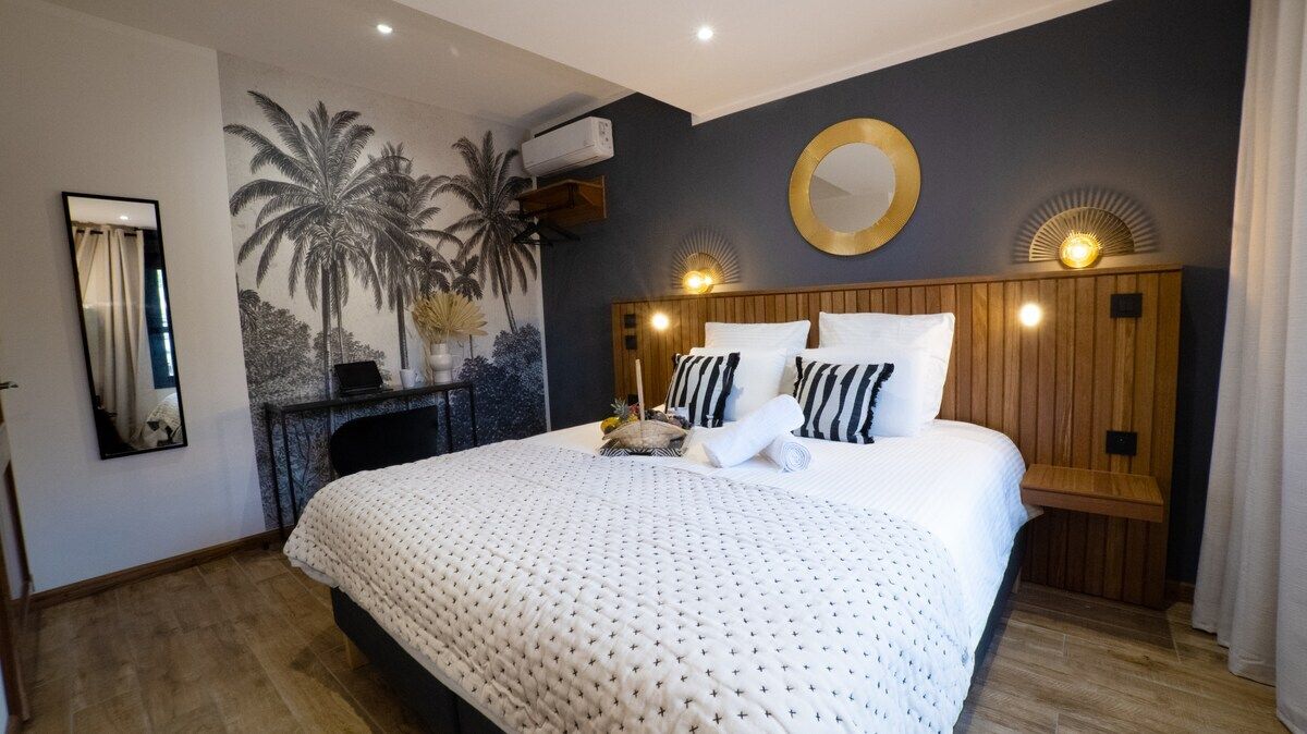 Un dormitorio con una cama grande, un espejo montado en la pared, un aire acondicionado también fijado a la pared y un mural decorativo.