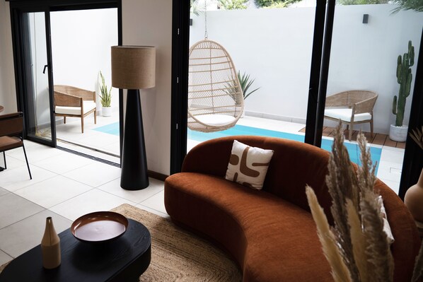 A living room with a sofa, a hanging chair, a lamp, and a view of a pool. - 10 Rue Du Four à Chaux (Saint-Denis)
