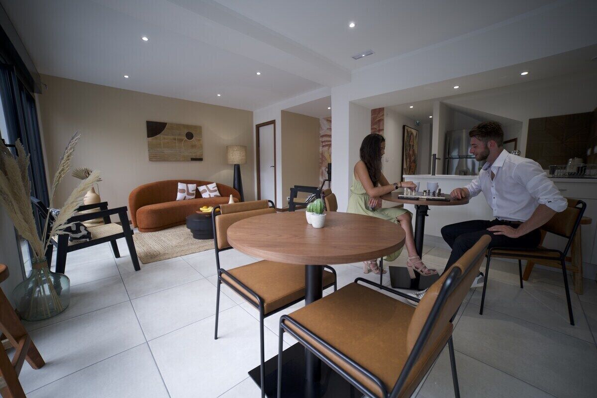 A modern living room with a round wooden table, two brown leather chairs, a sofa, and a coffee table.