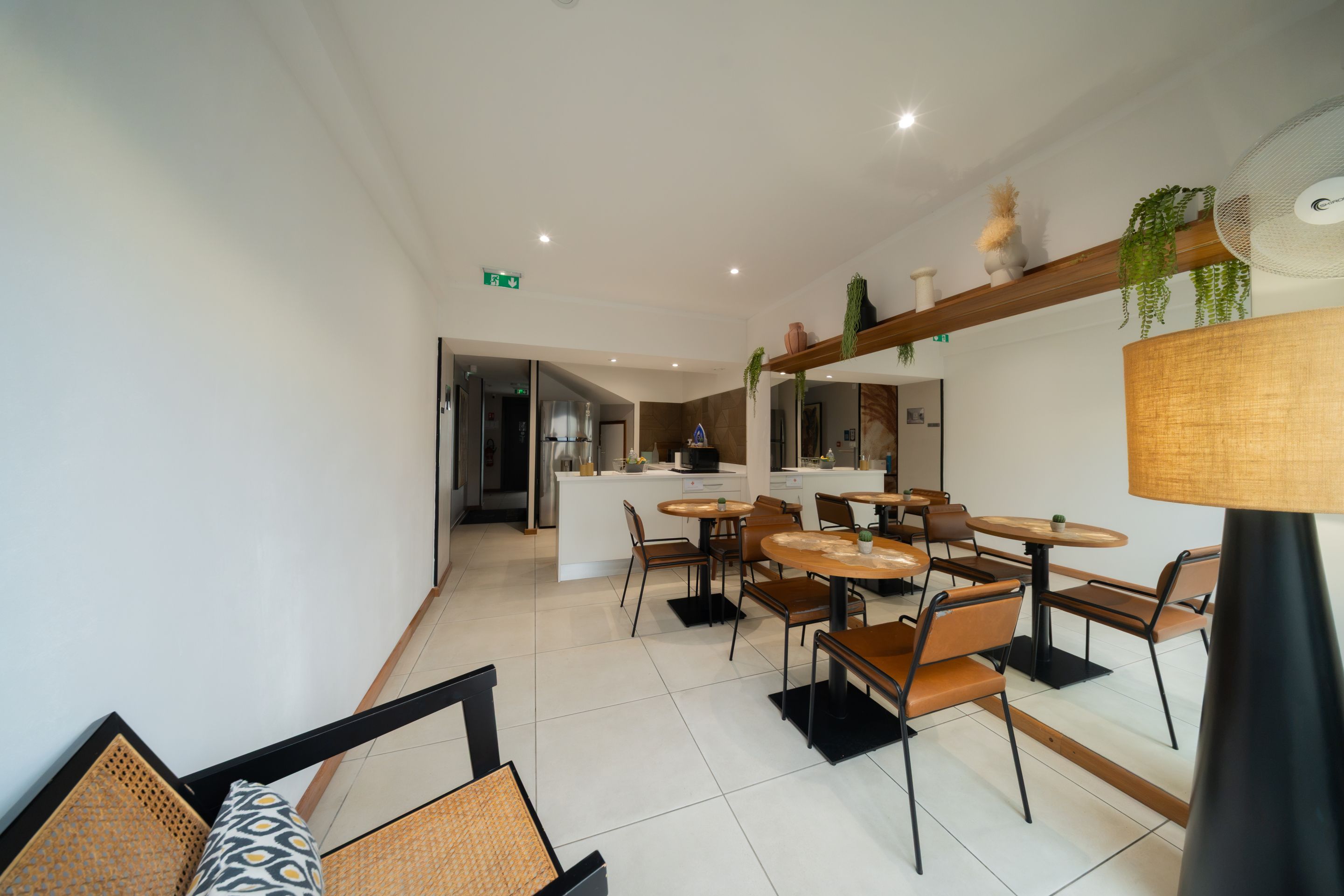A modern dining area with round tables and chairs, a kitchen in the background, and a ceiling fan.