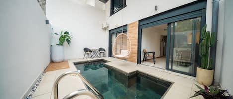 Un área de piscina moderna al aire libre con una piscina cristalina, un espacio de descanso con sillones y una planta en maceta.