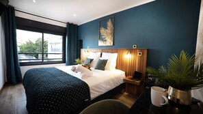 A modern hotel room with a large bed, a wooden headboard, a nightstand, a potted plant, and a view of the outdoors. - 10 Rue Du Four à Chaux (Saint-Denis)