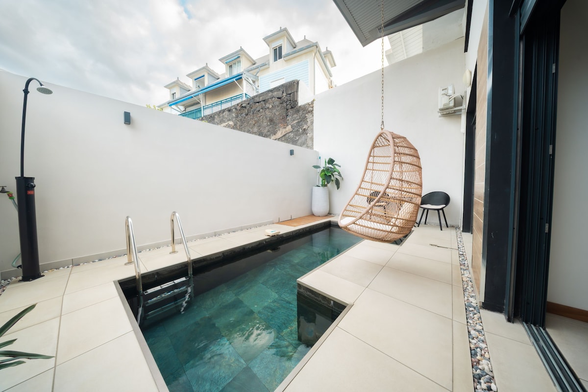 Una piscina con escalera, una silla colgante y una planta en maceta.