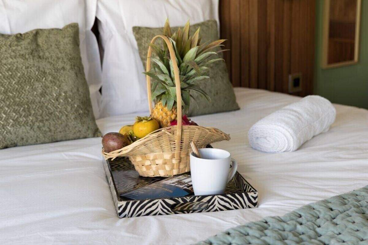 A neatly made bed with a woven tray holding fruits, a white mug, and a rolled towel.