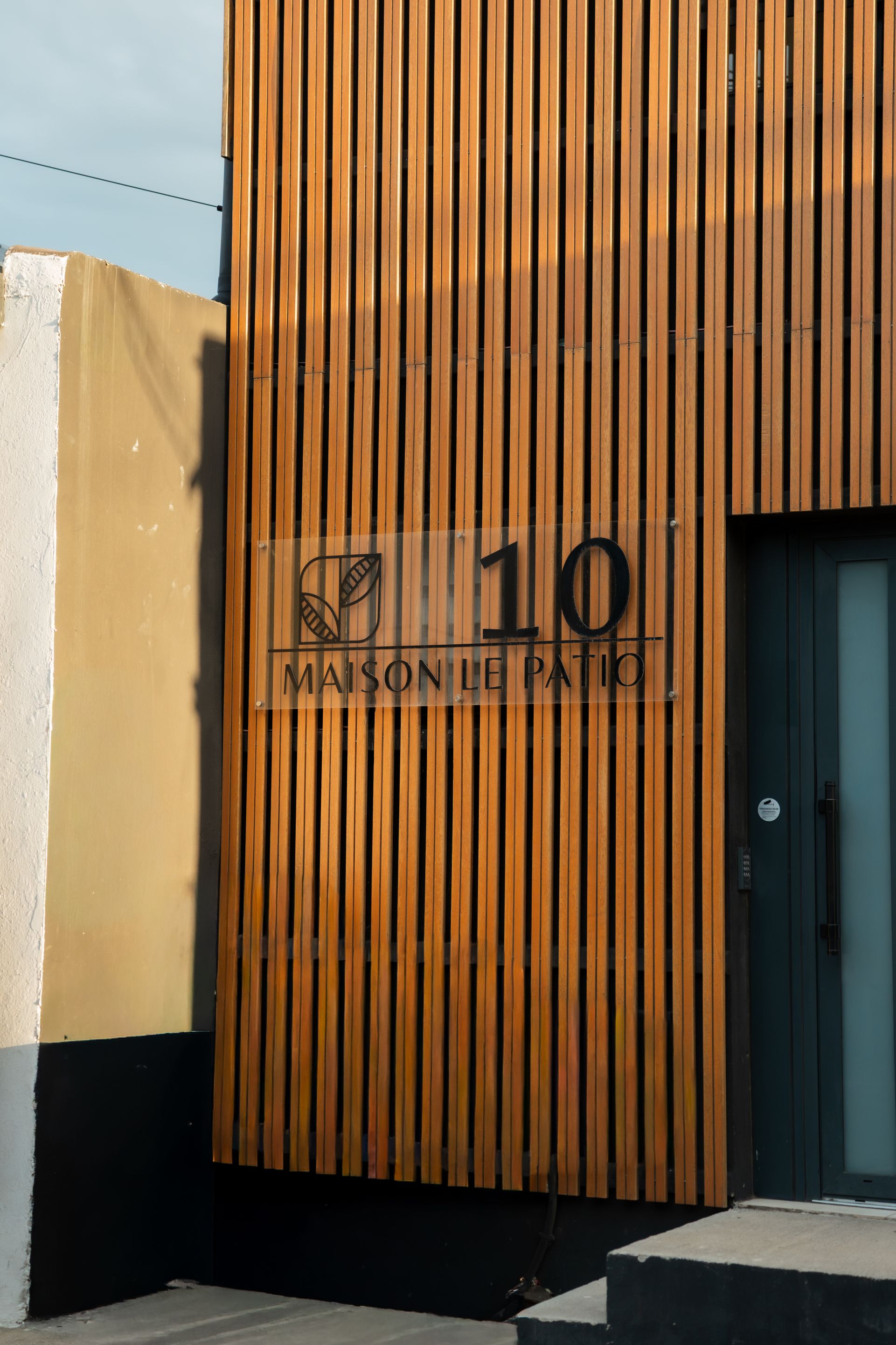 Fachada de edificio con listones de madera verticales y un letrero que dice 'MAISON LE PATRIC' con el número '10' encima.