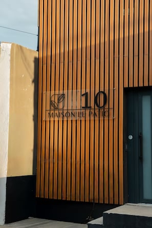 Fachada de edificio con listones de madera verticales y un letrero que dice 'MAISON LE PATRIC' con el número '10' encima.