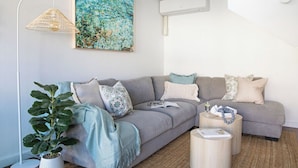 A modern living room with a grey sectional sofa, a potted plant, and a floor lamp. - By the Bay Batehaven - King, Queen, 2 x Singles. Opposite Corrigans Beach & Park (Batehaven)
