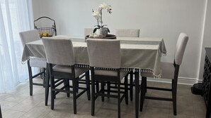 A dining area with a round table, six chairs, a chandelier, and a window with curtains.