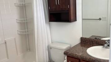 A bathroom with a shower, toilet, vanity, and a cabinet.