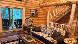 Interior de uma cabana de tronco com sofá de madeira, mesa de centro e escada.