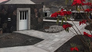 A stone building with a white door, surrounded by a paved area and red flowers. - EcoFunco (Santa Catarina do Fogo)