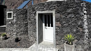 A stone building with a white door, a small window, and a solar panel. - EcoFunco (Santa Catarina do Fogo)