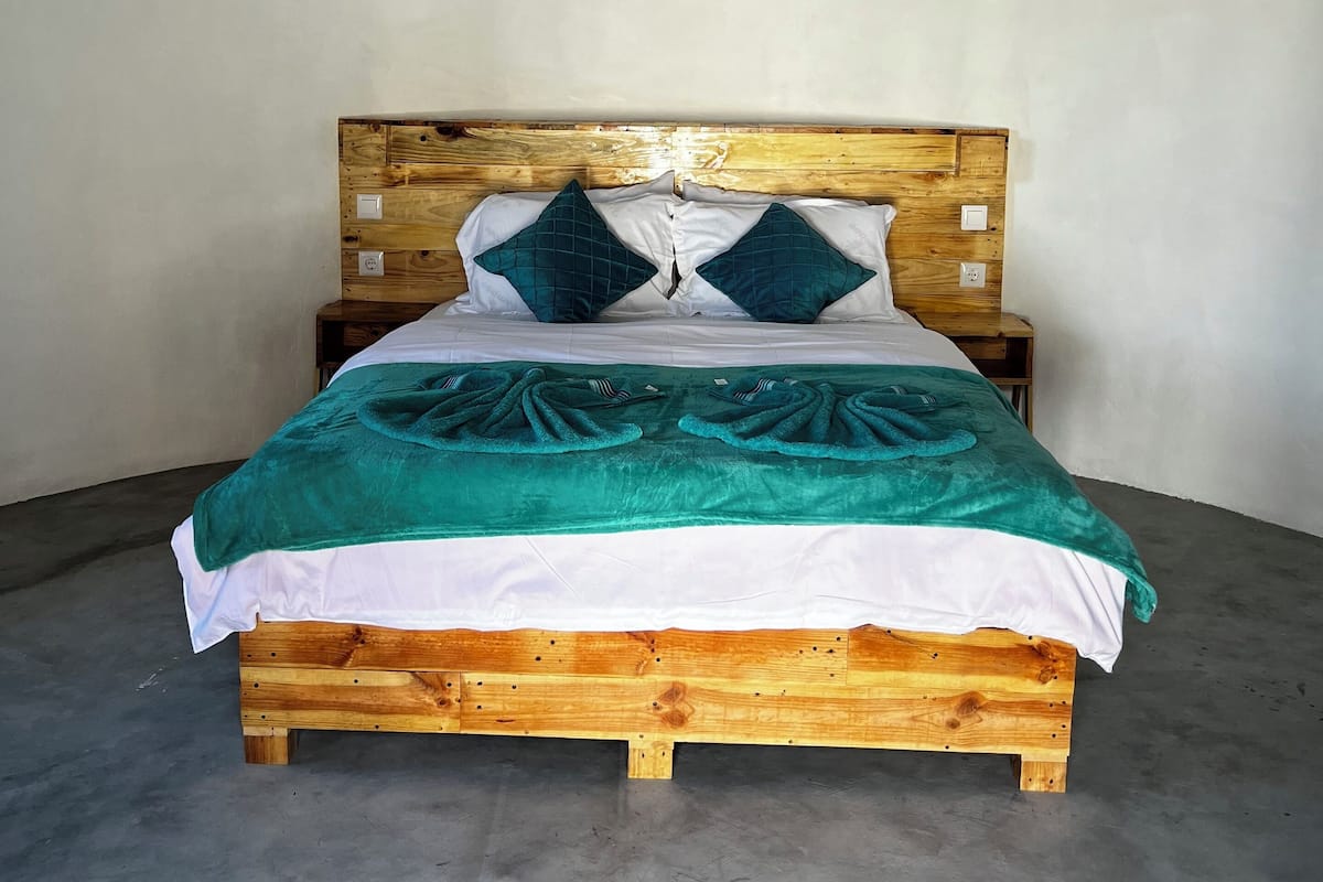 A wooden bed with a white and teal bedspread, two teal pillows, and a teal blanket.