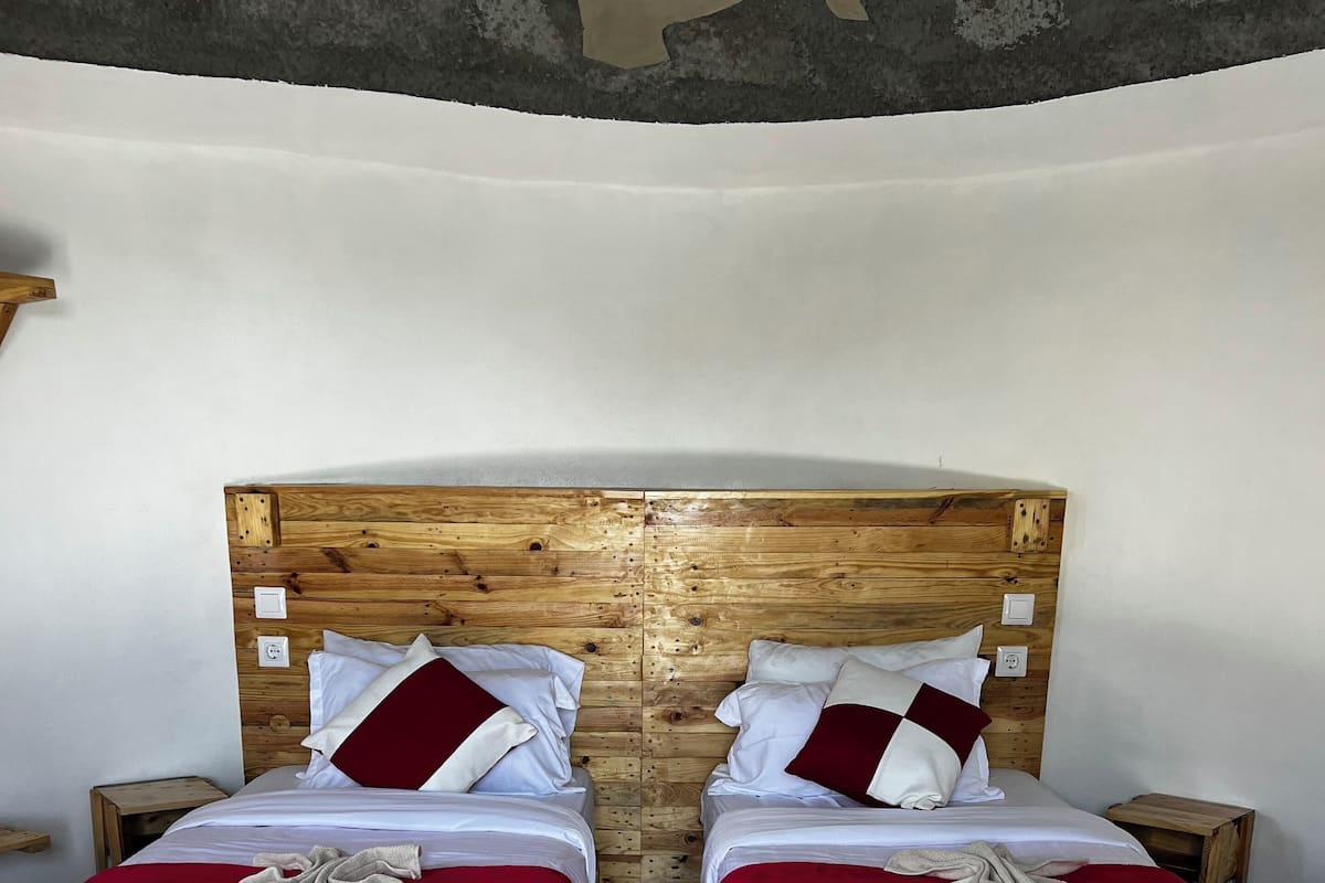 A room with two wooden beds, each with a red bedspread and white pillows, and a wooden headboard.