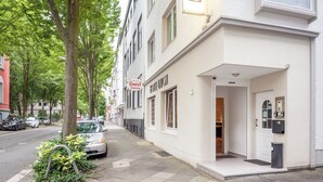 A hotel entrance with a white facade, a visible door, and a small garden area with a tree and plants. - Union Hotel by TM (Dortmund)