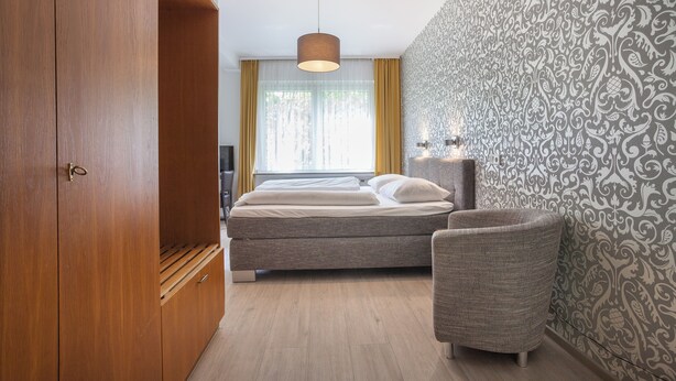 A bedroom with a bed, a chair, a wardrobe, and a patterned wall. - Union Hotel by TM (Dortmund)
