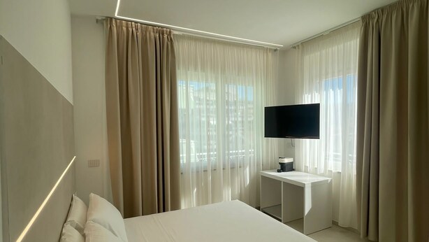 A modern hotel room with a large bed, a flat-screen TV, a small desk, and a window with curtains. - B&B Corso 219 (Montesilvano)