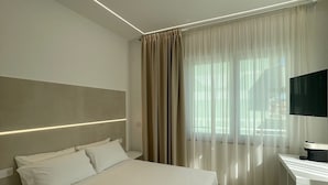 A modern hotel room with a large bed, a desk with a flat-screen TV, and a window with sheer curtains. - B&B Corso 219 (Montesilvano)