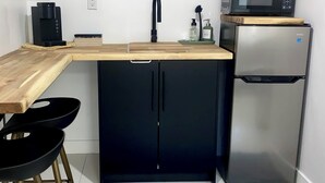 Una cocina compacta con encimera de madera, armarios negros, refrigerador de acero inoxidable, microondas y cafetera.