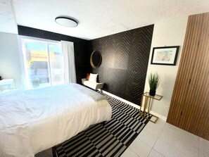 A modern bedroom with a large bed, a black and white striped rug, a round mirror, and a view of the outdoors. - Quiet, private suite with parking, steps away from the West Kelowna Wine Trails
 (West Kelowna)