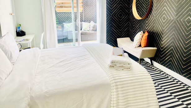 Una habitación de hotel moderna con una cama grande, un escritorio pequeño, una zona de estar con sofá y vistas a un espacio exterior a través de una puerta de cristal.