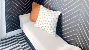 Una habitación con pared de patrón chevrón, un espejo redondo, un sofá blanco con cojín marrón y blanco, y una alfombra a rayas.
