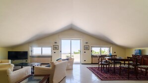 A spacious living room with a high ceiling, a TV, a sofa, a coffee table, and a dining area with chairs and a table. - VILLA PESCARA (Pescara)