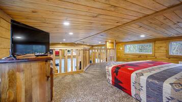 A wooden cabin interior with a bed, a television on a wooden stand, and a view through a door to an outdoor area.