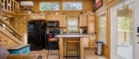 A compact kitchen with wooden cabinets, a black refrigerator, a stove, and a bar stool.