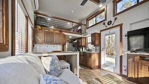A spacious living area with a sofa, a kitchen with wooden cabinets, a dining table, and a TV.