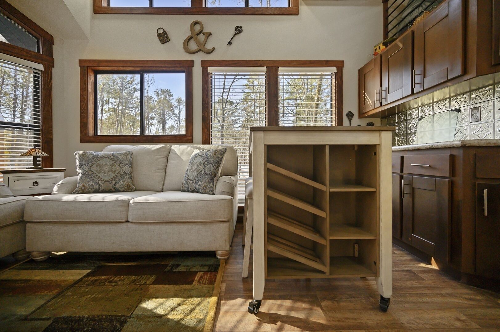 A cozy living room with a sofa, a wooden table, and a kitchen area with cabinets and a backsplash.