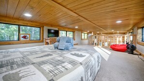 A spacious bedroom with a large bed, a blue chair, a red bean bag, and a TV on a wooden desk.