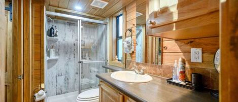 A wooden cabin bathroom with a shower, toilet, and sink.
