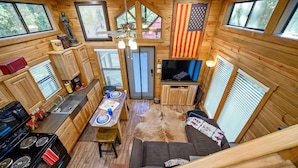 Una cabaña acogedora con cocina, comedor y sala de estar, con paredes de madera, televisor montado y una bandera.