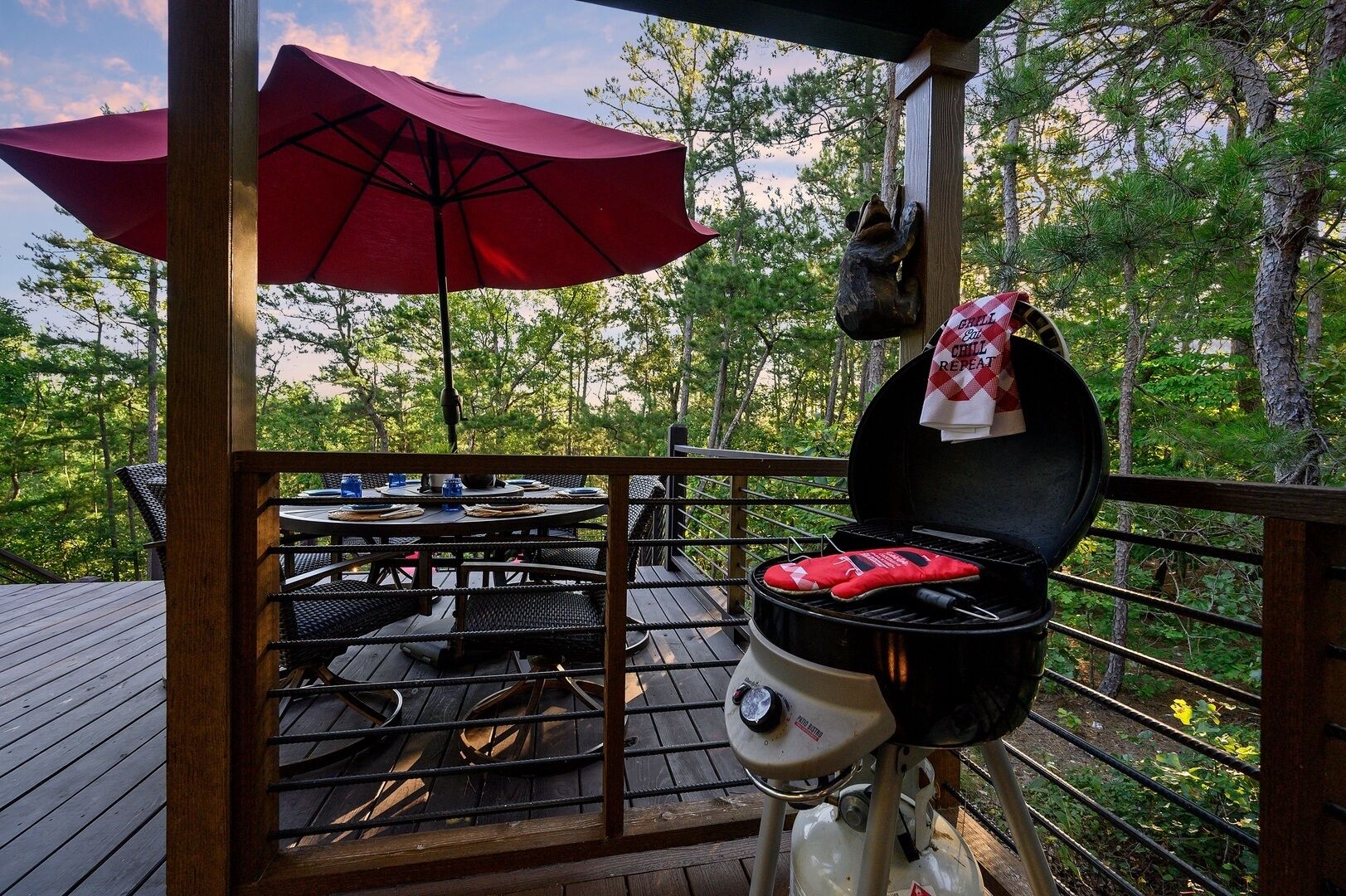 An outdoor deck with a grill, a table with chairs, and a red umbrella.