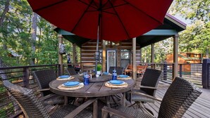 Un área de comedor al aire libre con una mesa redonda, sillas de mimbre y un paraguas rojo.