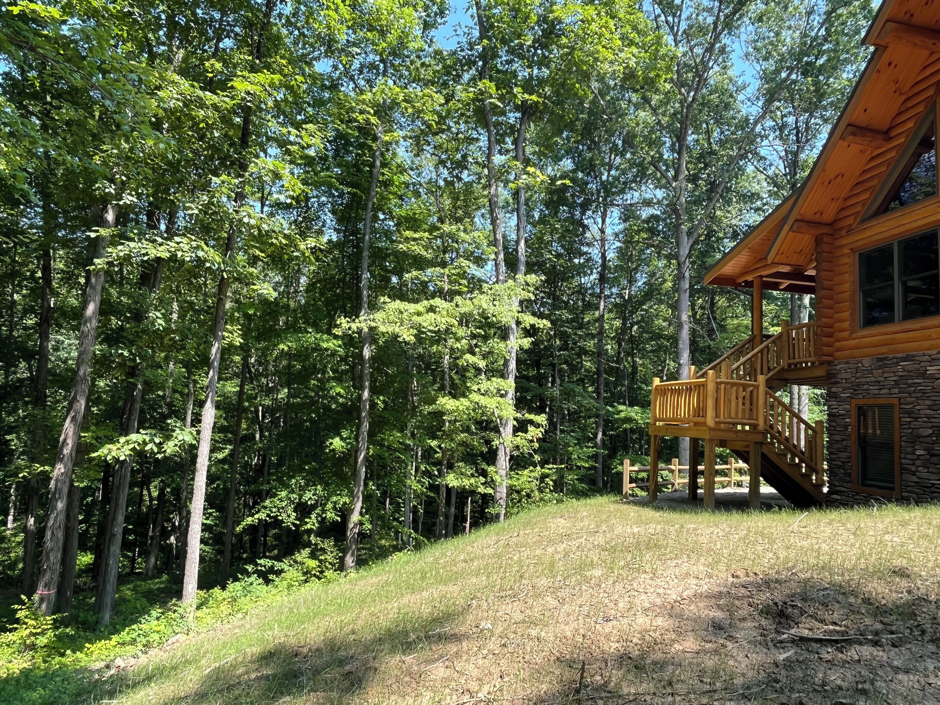 A cabin with a stone foundation and a wooden deck, surrounded by dense forest.