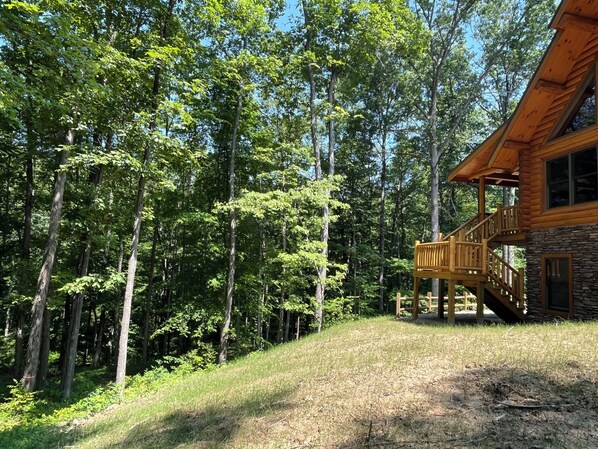 A cabin with a stone foundation and a wooden deck, surrounded by dense forest.