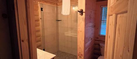 A wooden cabin bathroom with a glass-enclosed shower, a toilet, and a sink.