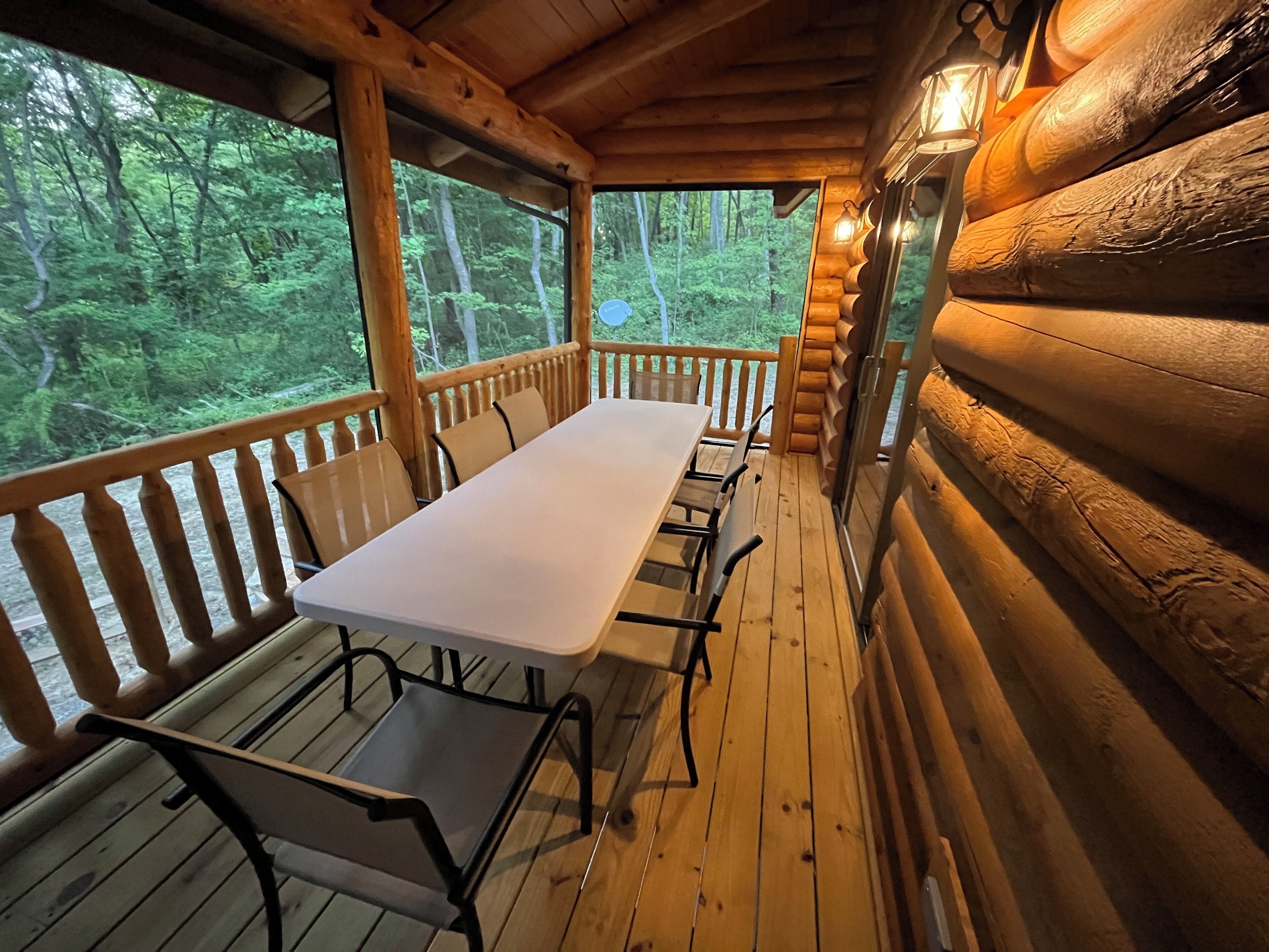 A wooden deck with a long table and chairs, surrounded by wooden railings, overlooking a forested area.