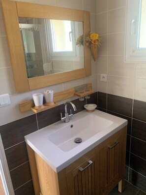 Een badkamer met een witte wastafel, houten kastjes, een spiegel en een klein plankje met toiletartikelen.