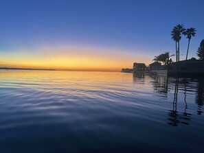 A calm waterfront at sunset with palm trees and a building with a balcony. - Clean & Relaxing 3 bedroom 2 bathroom Waterfront home. (Hudson)