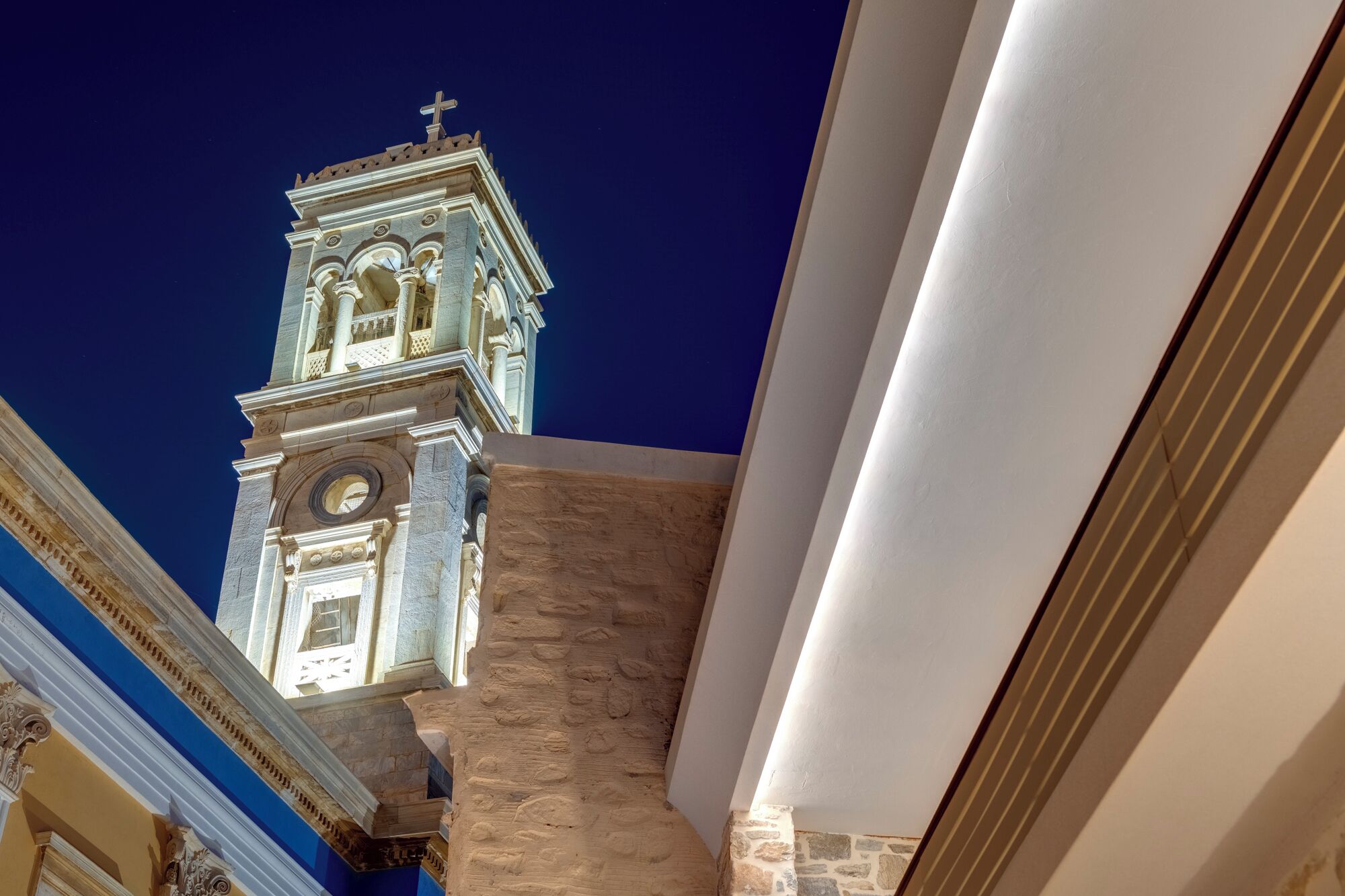 A church tower with a cross on top, a clock, and a bell.