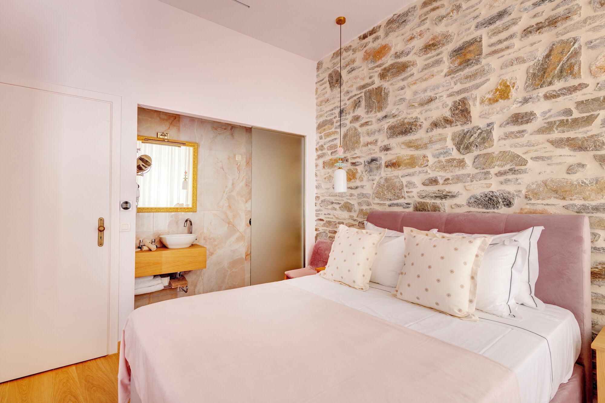 A bedroom with a stone wall, a bed with white bedding, and a wooden nightstand.