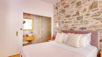 A bedroom with a stone wall, a bed with white bedding, and a wooden nightstand.