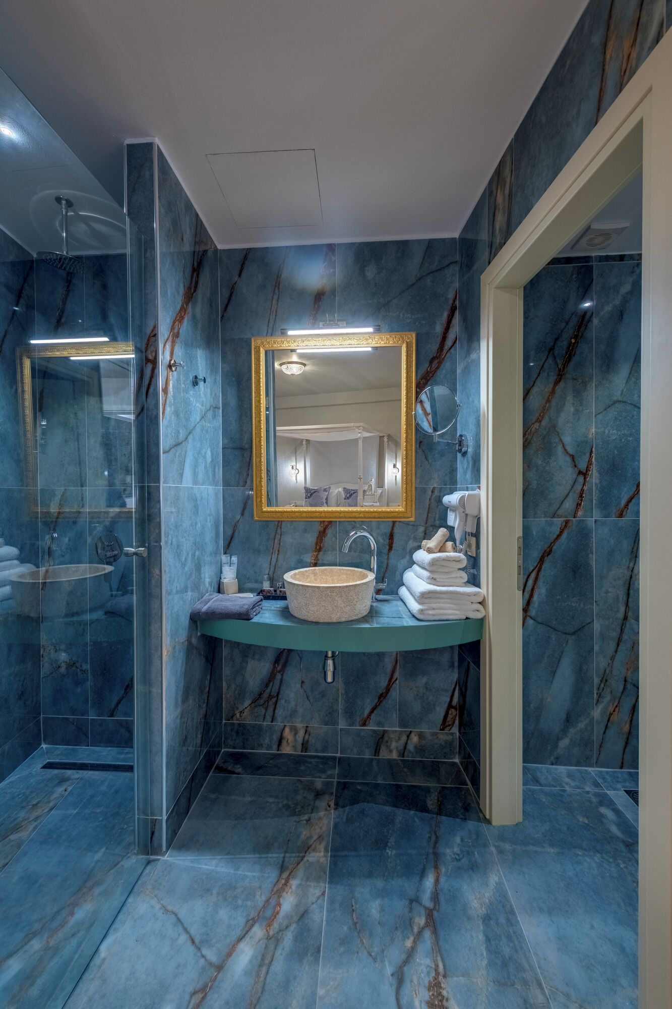 Un baño moderno con suelo de mármol, un lavabo redondo y un espejo grande con marco dorado.